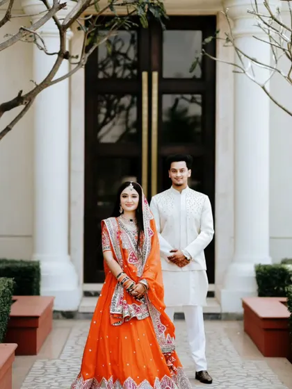 A classic portrait of the couple in front of an elegant doorway. The bride's vibrant orange lehenga provides a beautiful pop of color.