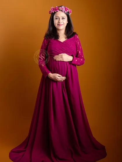 A radiant solo portrait of a mom-to-be wearing a floral crown and a magenta gown against a warm, golden studio backdrop.