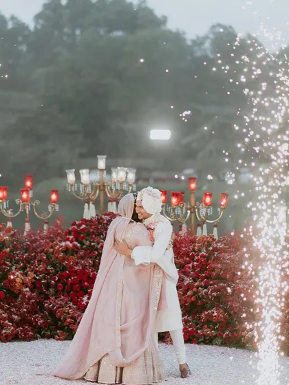A tender embrace with sparklers adding to the magic. The dense red floral backdrop creates an intensely romantic and celebratory setting.