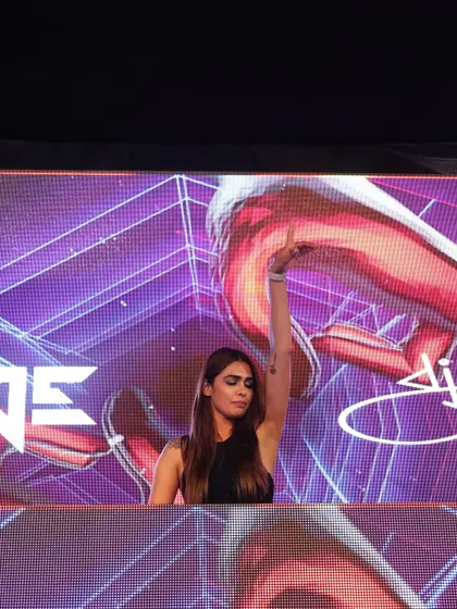 A stunning shot of me at a Delhi wedding, with one hand raised as the beat drops. The vibrant purple visuals on the LED screen behind me add to the festive atmosphere.