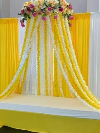 A beautiful floral canopy setup for a Haldi or Mehndi ceremony. We used cascading strings of yellow and white flowers to create a tent-like structure over the seating, with a simple yellow and white drape backdrop.