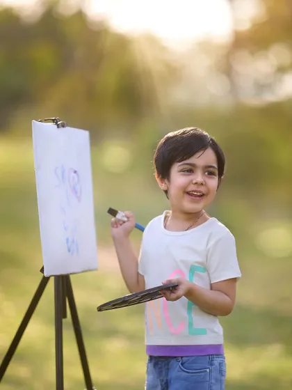 A smile of creative satisfaction. The golden sunlight filtering through the trees adds a beautiful, warm glow to this little artist's outdoor portrait session.