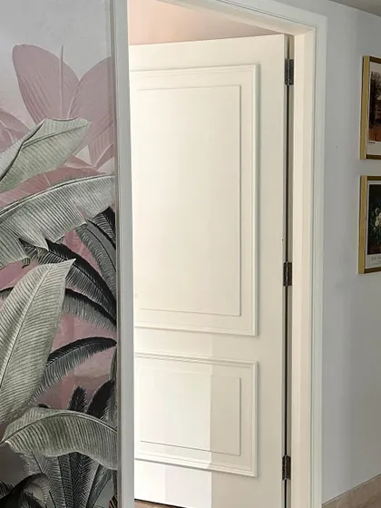 A classic white paneled door stands in beautiful contrast to the adjacent wall covered in a soft, botanical wallpaper.