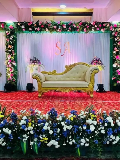 A classic and grand reception stage setup. This design features lush floral borders, elegant white and green drapery, and a custom monogram to personalize the backdrop for the happy couple.