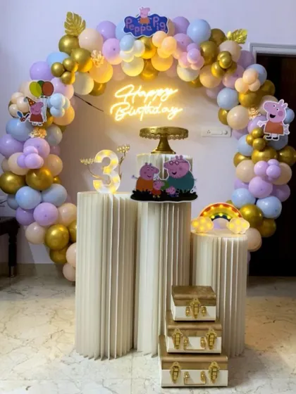 A closer view of the Peppa Pig themed birthday setup, showing the cake and props on the plinths under a pastel balloon arch.