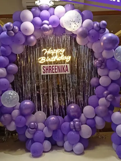 A beautiful purple-themed birthday party with a full circular balloon arch, a silver sequin backdrop, and a neon sign for Shreenika's celebration.