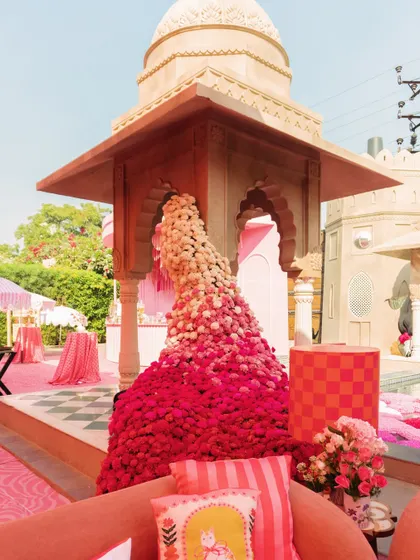 A floral waterfall of pink and red blooms cascades from a traditional chhatri, blending heritage architecture with a vibrant, modern color palette.