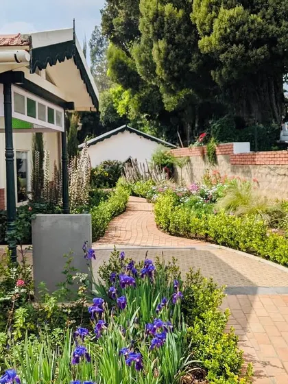 A pathway lined with purple irises and other flowers, leading towards one of the colonial-style buildings.