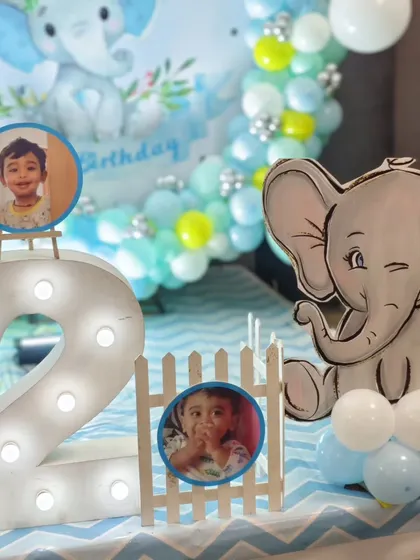 A close-up of a baby elephant-themed second birthday, with a large marquee number '2' and personalized photo cutouts of the birthday boy.