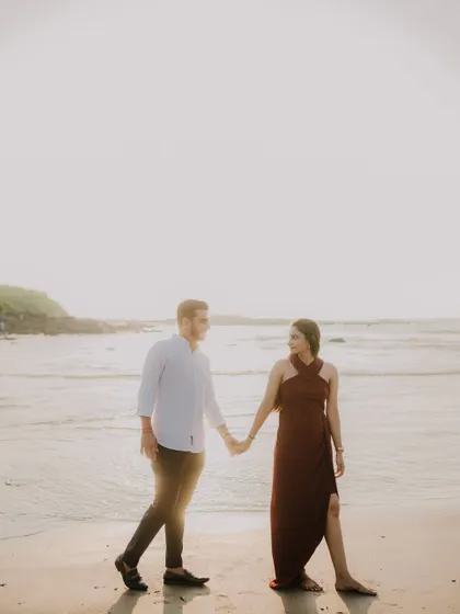 A wide shot of the couple holding hands on the beach. The vastness of the sea and sky creates a beautiful, serene backdrop for their pre-wedding portrait.