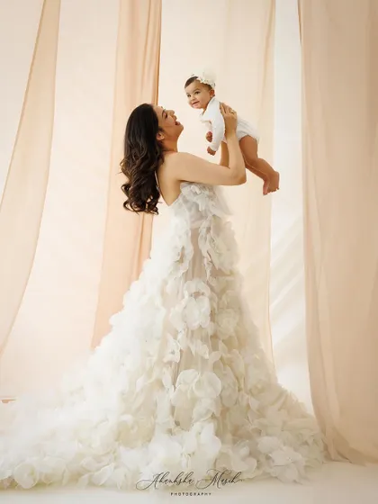 A joyful mother lifts her baby, both dressed in beautiful white. This portrait captures a moment of pure, unscripted happiness.