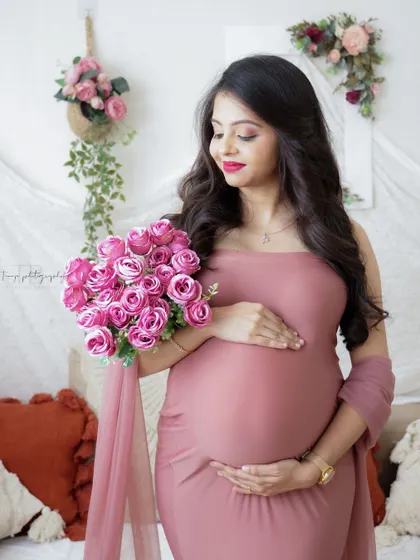 A beautiful and serene portrait in a boho-chic setting. The mom-to-be holds a bouquet of pink roses, her dusty pink gown perfectly complementing the scene.