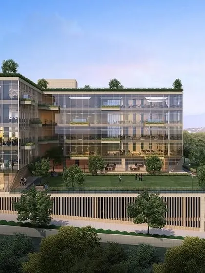 A different perspective of the commercial building in Navi Mumbai, showing its L-shaped form and the integration of green lawn spaces. The transparent glass façade allows for ample natural light, creating a bright and productive work environment.