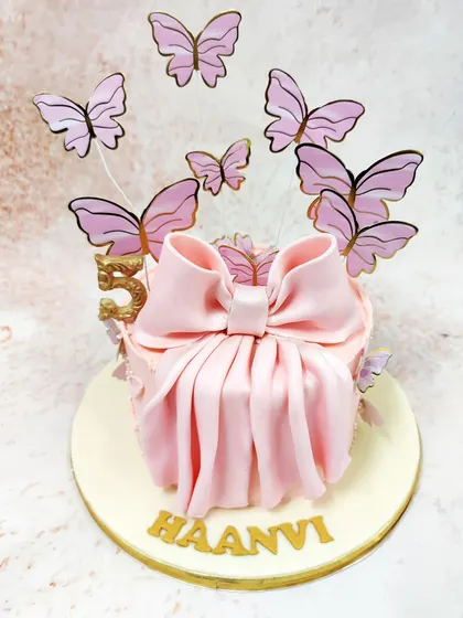 We present a gift of pure elegance with this pink bow cake. A large, beautifully draped fondant bow is the centerpiece, surrounded by a flight of ethereal pink and gold butterflies, making the cake itself look like a precious, unopened present.