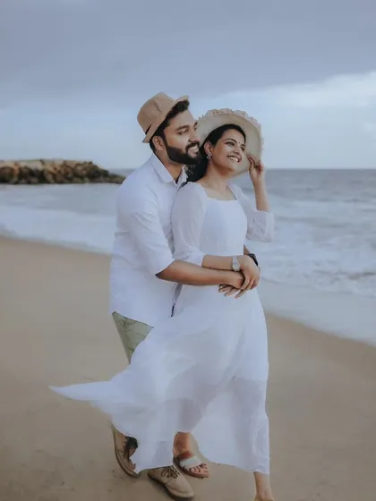 A breezy, romantic beach pre-wedding shoot, with the couple enjoying the sea and sand in coordinated white outfits.