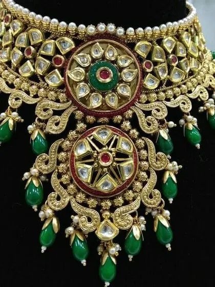 A detailed product shot of a Jadau-style choker. The intricate floral motifs with red and green stones make this a centerpiece of any bridal collection.