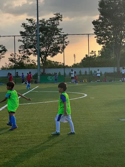 As the sun sets, the energy on the field stays high. Young players in bright green bibs participate in a small-sided game, a perfect way to apply the skills learned during our evening kids football practice.