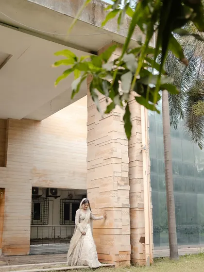 A wide, architectural shot of the bride standing against a modern stone building, creating a beautiful contrast with her traditional attire.