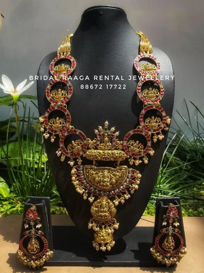 A unique and artistic temple jewellery set. The design features circular motifs with Goddess Lakshmi carvings, all studded with red Kemp stones.