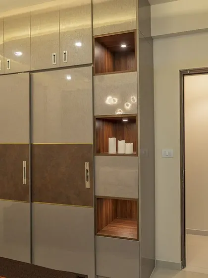 This two-toned sliding wardrobe in brown and beige features a sleek design with integrated handles. The adjacent open shelving unit is perfect for displaying decorative items.