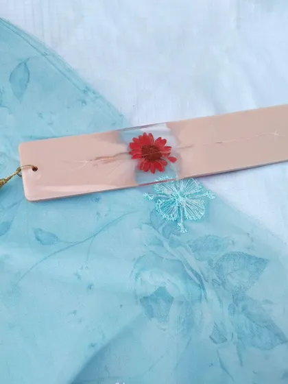 Another angle of the red flower bookmark, showing its slim profile and the delicate white tassel.