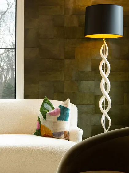 A close-up of a sofa in a lounge featuring our 'Appaloosa' wallpaper. The colorful, abstract-patterned cushion adds a playful pop of color, contrasting beautifully with the deep green, textured walls.
