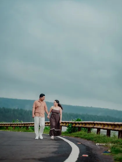 A wide shot of the couple walking hand-in-hand on a road with a beautiful view of the Kokan hills and backwaters, telling a story of a journey together.