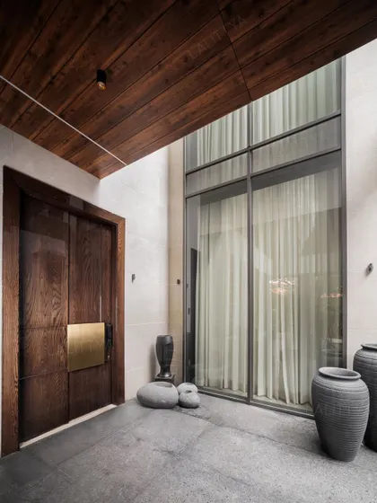 Our work isn't just about interiors; we are architects who shape spaces from the ground up. This modern entrance, with its bold wooden door, brass accents, and double-height window, establishes a sense of arrival and sets the tone for the quiet luxury within.