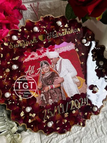 An 8-inch round frame with a zigzag edge, filled with deep red varmala petals and gold flakes. The couple's photo, names, and wedding date are placed at the center.
