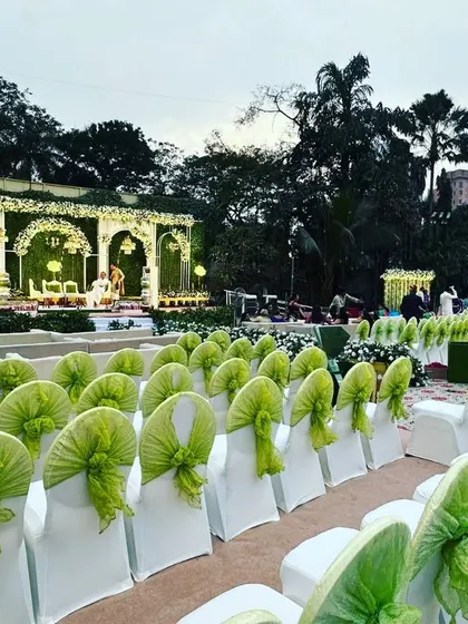 A wide view of an elegant outdoor wedding reception at The Acres Club lawns. The grand stage is complemented by neat rows of seating with lime green accents, ensuring every guest has a great view.