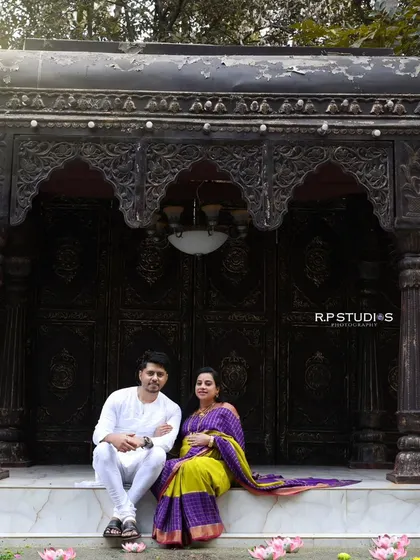 A wide shot showing our traditional outdoor-style setup. The intricately carved doorway provides a stunning backdrop for this couple's portrait in ethnic wear.