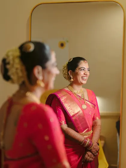 A reflection shot capturing the bride's happiness. The traditional South Indian look is complete with a neat bun adorned with sun and moon symbols.