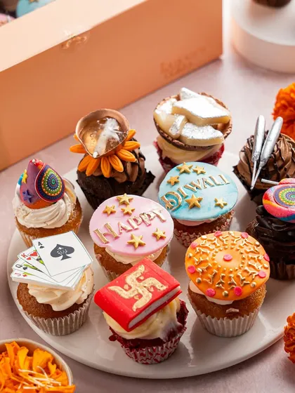 A box of twelve mini cupcakes, each with a unique Diwali-themed topper, including playing cards, diyas, and festive greetings. These are perfect for parties and sharing the festive joy in bite-sized form.