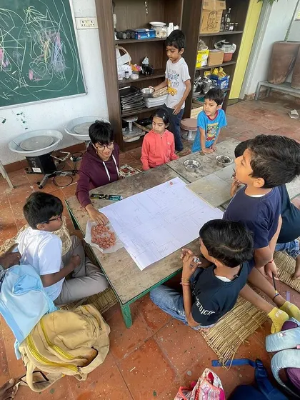 A group of young learners gathered around a large sheet of paper, planning their sustainable marketplace design. This is collaborative, project-based learning in action.