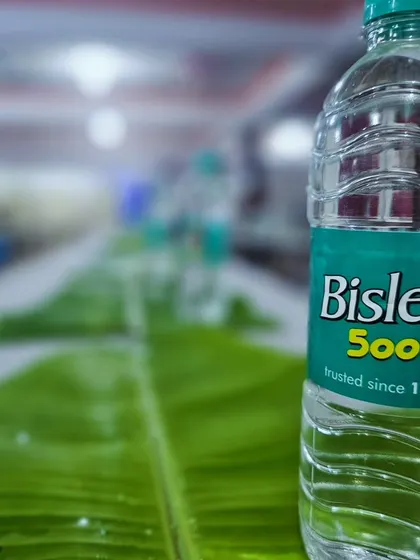 A close-up of a fresh banana leaf and a bottle of water, representing the simple and clean start to our traditional meal service.