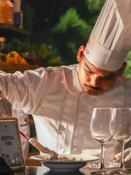 A chef meticulously plates a "Risotto Al Funghi". The focused effort highlights the high standards of our culinary team and the artistry involved in our live cooking stations.