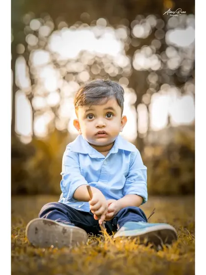 A beautiful, warm-toned portrait of Ivaan sitting in the grass. The soft, out-of-focus background makes his curious expression the center of attention in this outdoor shot.