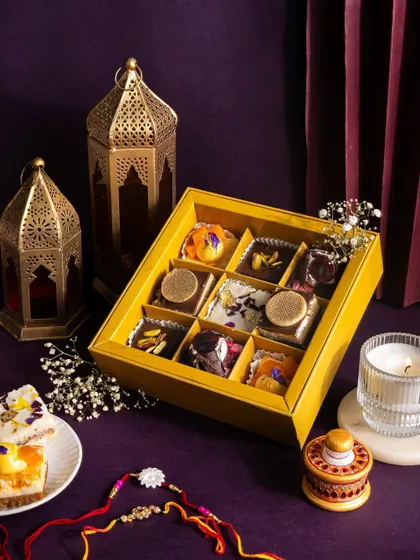 A moody and elegant shot of a Rakhi sweet box, using a deep purple background and lanterns to create a luxurious, gift-worthy feel.