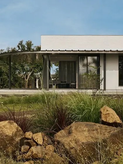 The exterior of Pavilion House showcases a blend of materials, including white brick, dark stone, and expansive glass, all nestled within a resilient desert garden. The low-lying form respects the landscape, ensuring the home feels like a natural part of its environment.
