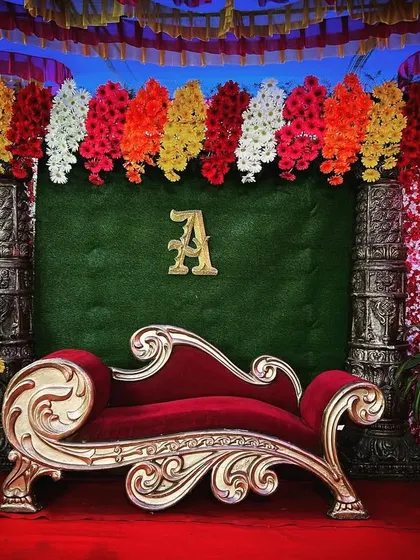 We offer simple yet elegant decor packages for events like engagements or naming ceremonies. This stage features a classic red and gold theme with a comfortable diwan, floral pillars, and a custom initial.