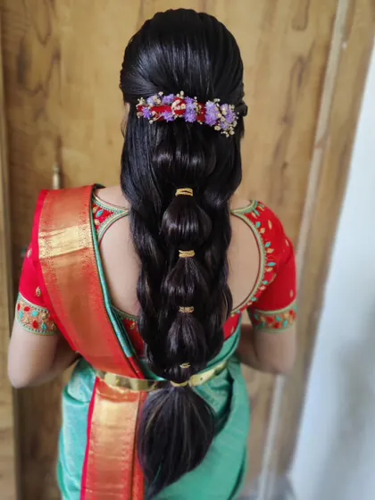 A modern take on a bridal braid. This bubble braid is decorated with a floral hair accessory, offering a chic and stylish option for a reception or sangeet.