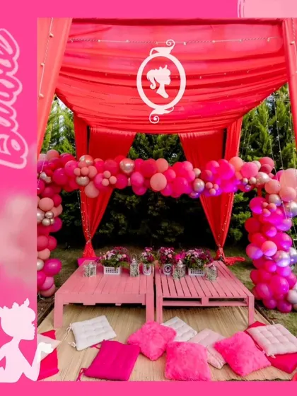 The full view of the pink kids' seating area, complete with a Barbie silhouette logo, fluffy pillows, and themed table decor.