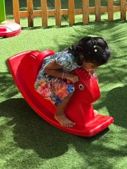 A young girl enjoys a ride on a rocking horse in our safe, outdoor play area. Free play is crucial for social and physical development.