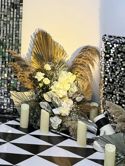 A close-up of the floral arrangements for the cocktail party, featuring dried pampas grass, golden palm leaves, and white roses, all illuminated by pillar candles.