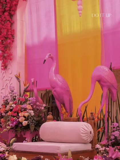 A quirky and fun seating area for the bride and groom, featuring pink flamingo statues and a backdrop of ombre pink and yellow drapes. This design was all about embracing a playful, tropical vibe.