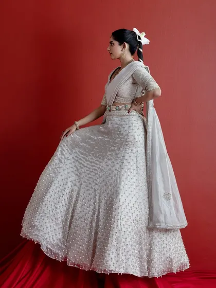 A side profile of the ivory lehenga, highlighting the elegant silhouette and the unique draping of the dupatta. This angle provides a clear view of the embroidered belt that cinches the waist and adds a touch of modern structure.