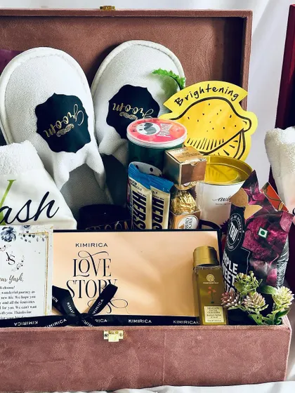 A close-up of the ultimate groom hamper. It features personalized "Groom" slippers, a monogrammed towel, a "Love Story" gift set, and a selection of his favorite snacks and chocolates.