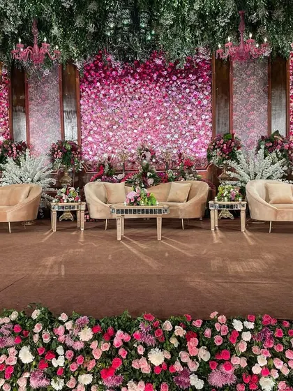 The main stage for the regal wedding, featuring a stunning backdrop made entirely of fresh pink and white roses. The plush, neutral-toned furniture was chosen to complement the vibrant floral wall, creating a perfect setting for photographs.