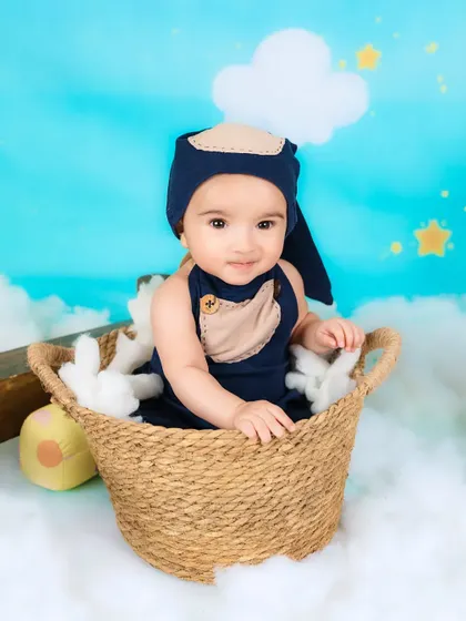 A baby boy sits in a basket, ready for a ride in his hot air balloon through the clouds.