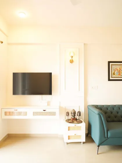 A minimalist living room with a floating white TV unit and a comfortable teal sofa. The wall-mounted sconce and decorative molding add a touch of classic elegance.